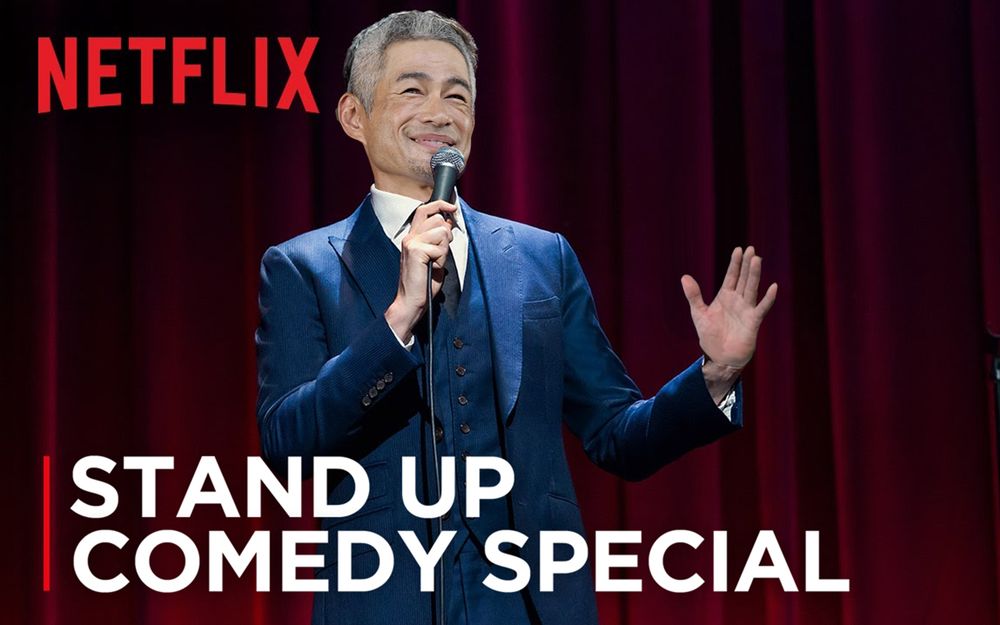 Ichiro Suzuki in a suit with a mic in front of a red stage curtain with the Netflix logo and words reading "Stand Up Comedy Special"