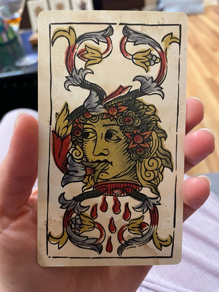 A gold-colored head in profile, like one would see on a coin, except the head is severed and bleeding from the neck