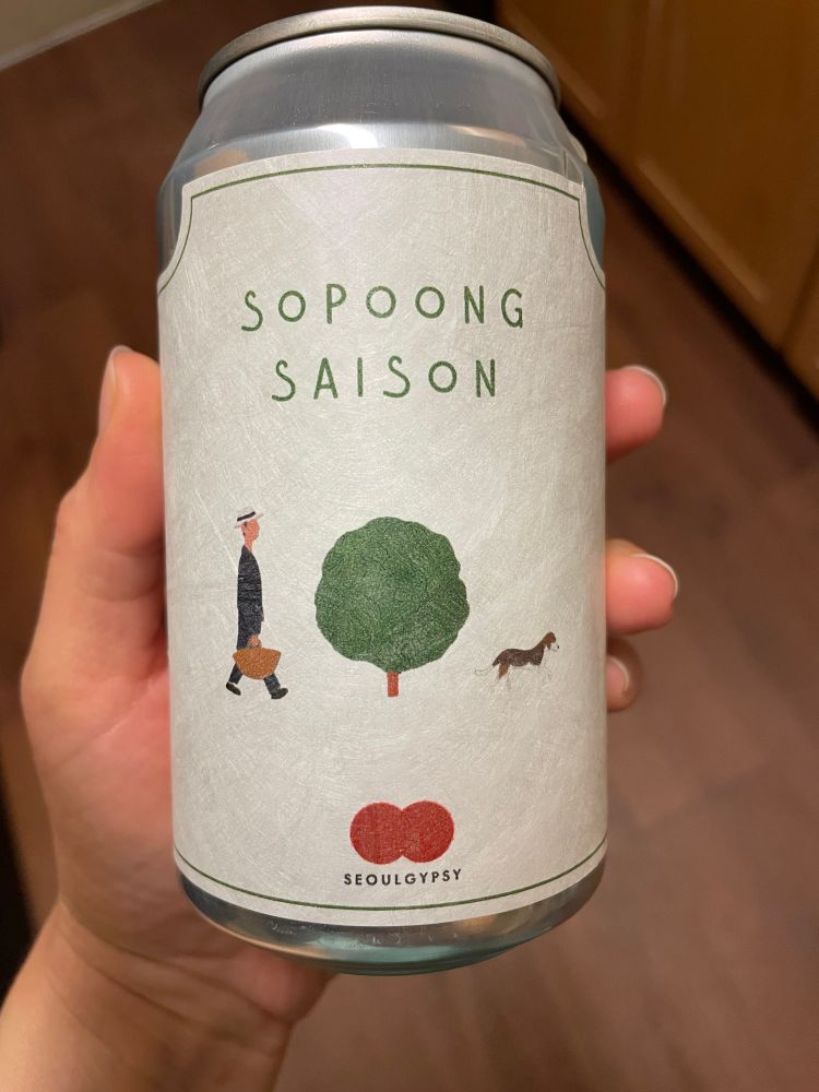 A can of Sopoong Saison from the Korean brewery Seoul Gypsy. Minimalist parchment label showing an illustration of a man with a picnic basket, a tree, and a beagle