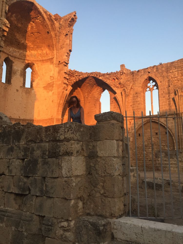 Sunlit ruins, with arches, woman with brown hair blowing across her face.