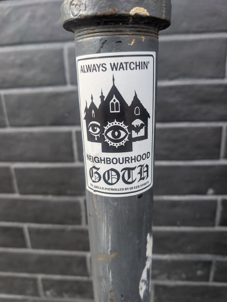 A sticker on a metal pole in Toronto. "Always Watchin' - Neighbourhood Goth. This area is patrolled by queer spirits."