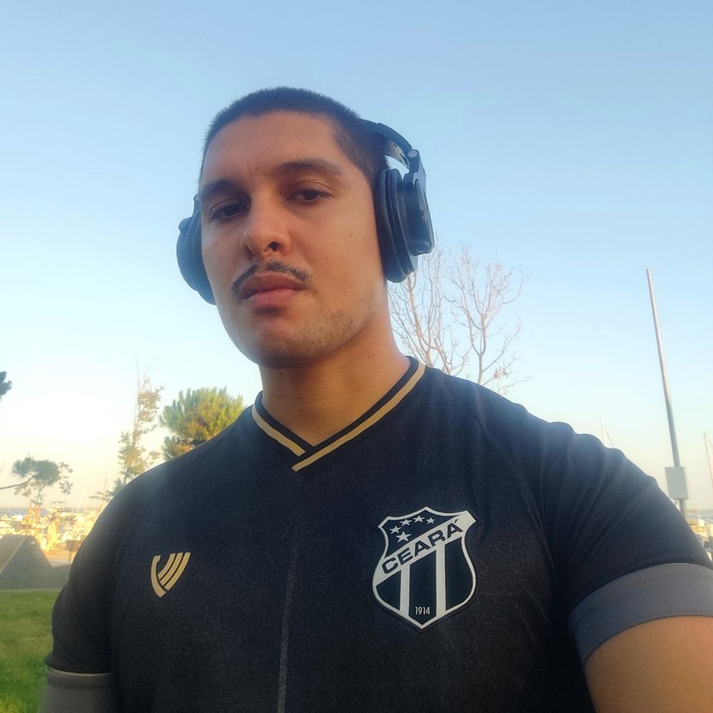 Selfie meu do peito pra cima, uso a blusa do Ceará S.C. e um headphone.