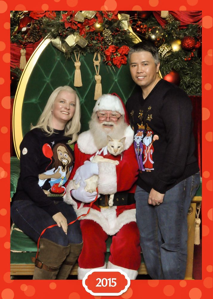 A couple & their cat posing for a Christmas photo with Santa Claus.