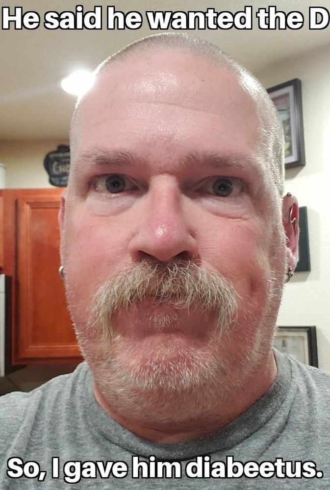 Buzz with a clipper cut, walrus mustache, and stubble beard. The image is captioned, 