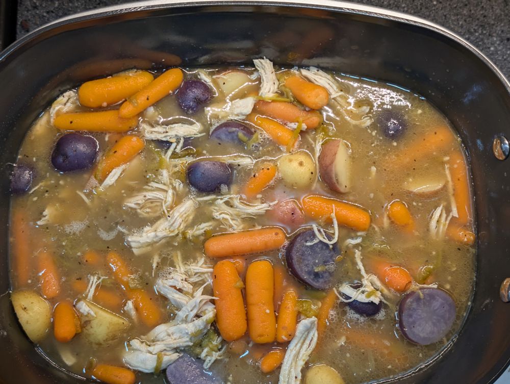 A batch of green chile stew. It contains carrots, various colors of potatoes, shredded chicken, and green chile. 