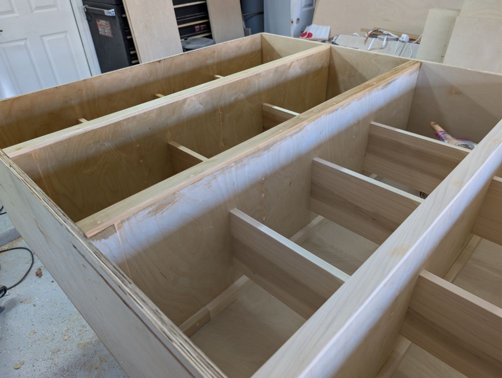 View of a wood cabinet for holding vinyl records. It's laying on its back. Two of the five compartments have a polyurethane finish applied.