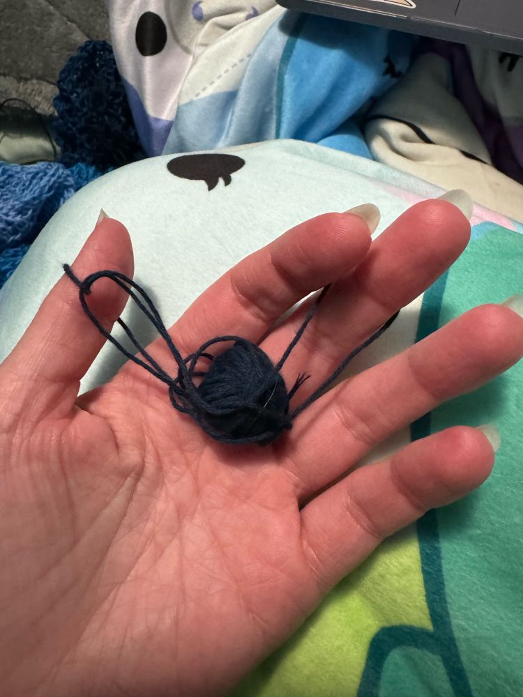 The palm of a person's left hand is visible with a quarter-sized ball of dark blue lace yarn