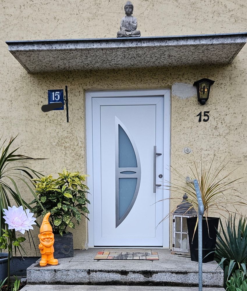 Picture of a front door. Above the door a buddha/zen statue, next to the door a statue of a garden gnome giving the middle finger. 