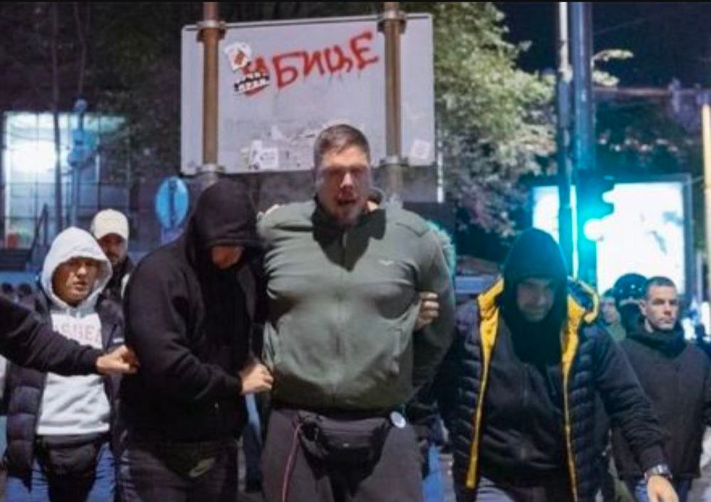 Vladimir Štimac wird von Polizisten in zivil (schwarze Hoodies) verhaftet, seine Hände sind hinten seinem Rücken, wahrscheinlich in Handschellen