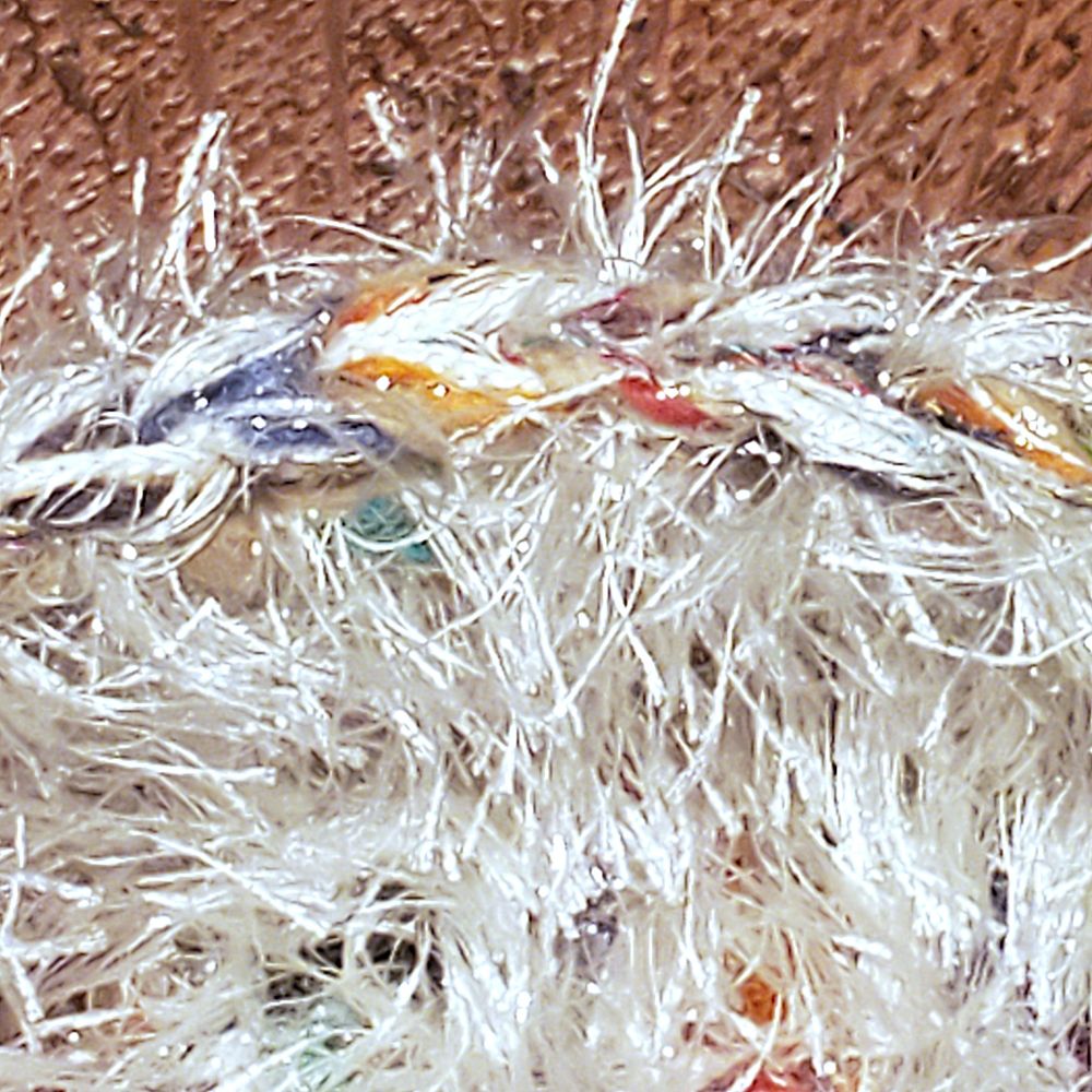 Looped edging on a fiber art piece.  Fuzzy, furry texture of white yarn with black, blue, orange, yellow, red rainbow color, againt brown oak.