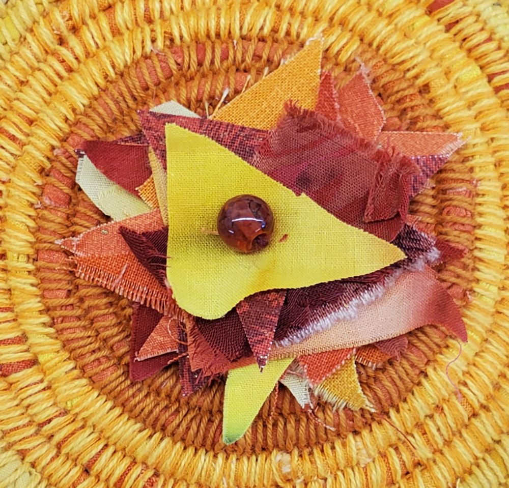 Lid of "Fire Energy" coiled vessel of upcycled, recycled gold, orange and red cloth and yarn contains and radiates the raw, burning intense heat of elemental fire, peaking in flames of fabric clippings with a crown of orange and red glass beads.
5.25” Diam x 2.5”H
(2024)
Original Work by Amy C Lund 