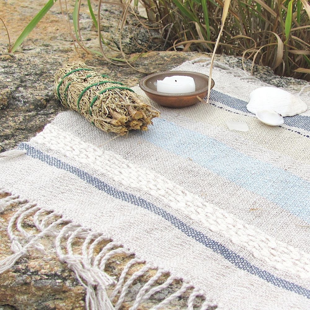 Artisan Handmade Woven Altar Cloth, with Ocean Blue, Sky Blue, Sandy Beige Gray, and White Textured Stripes, For Soothing Relaxation, Zen Serenity, Tranquility, Peaceful Meditation by Amy C Lund. Styled on a Beach with Cedar Smudge Stick, Small White Candle on A Copper Dish, Shells, with Sea Grass in the Background