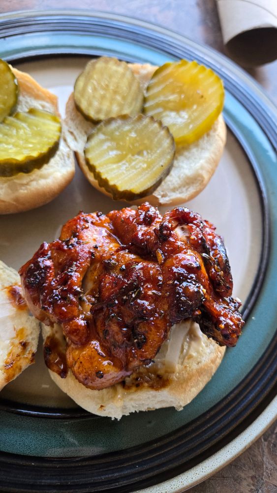 chicken thigh, charred and covered in a hot honey glaze. sitting atop a bottom bun, mayo, and onions. on the other bun, famous dave's devil's spit sweet pickles.
