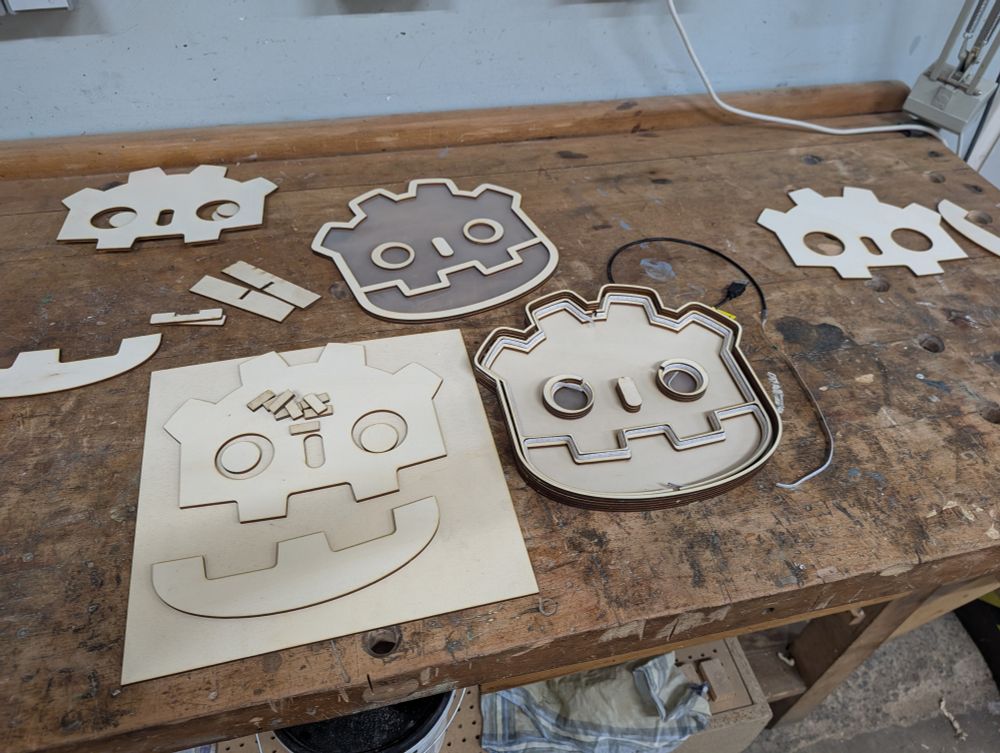 Individual parts of the Godot shaped lamp before assembly on a workbench. A led strip is lining the inside walls of the lamp. The top cover is still sitting next to the lamp frame and waiting for final assembly.