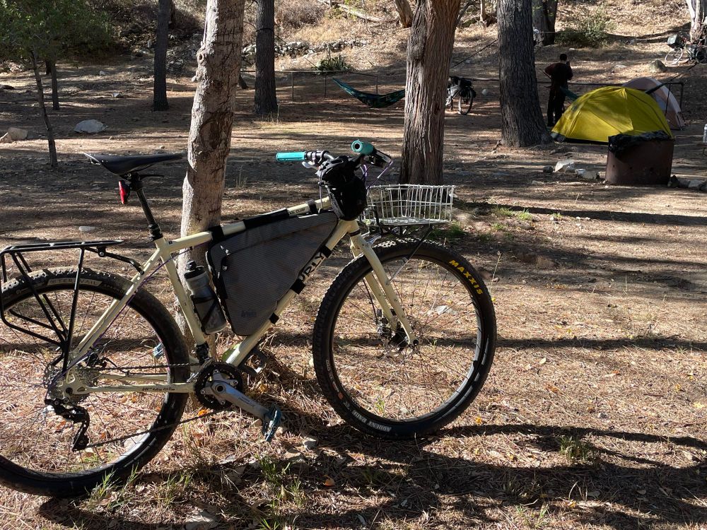 Bike against a tree with more trees and a yellow tent in the background. 