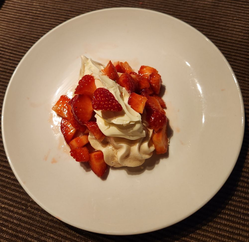 Une assiette avec une meringue de la double crème et des fraises coupées en petits morceaux