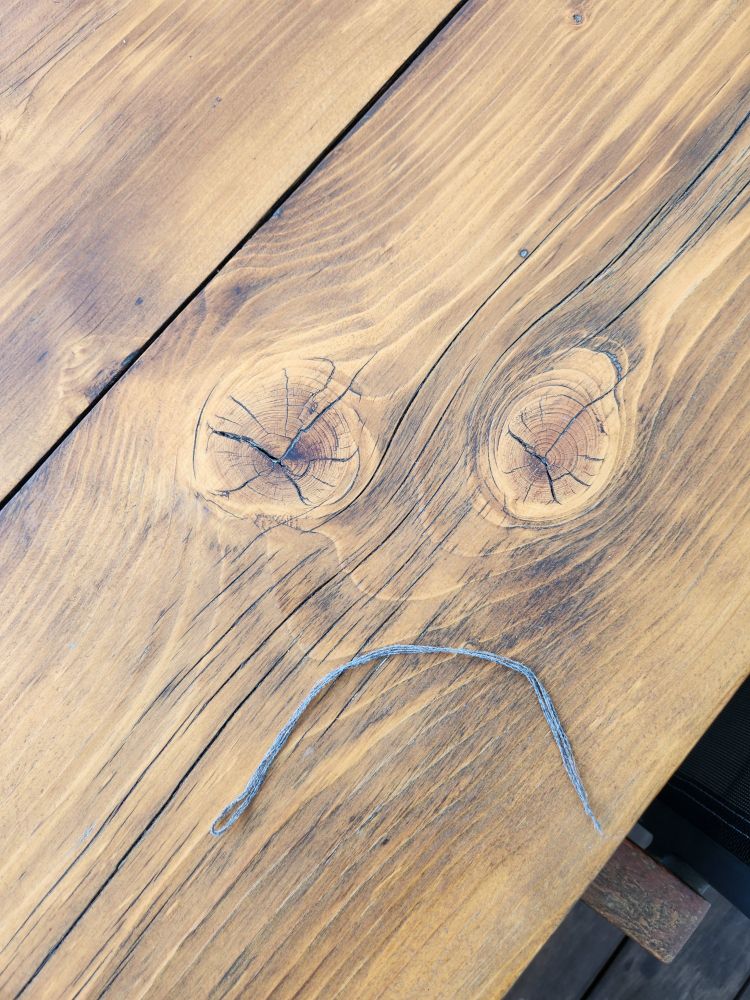 2 noeuds dans une planche en bois, 1 fil de laine, 1 visage triste
