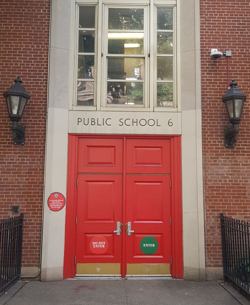 Une entrée d’école à NewYork avec une double porte rouge. Porte de droite avec panneau 