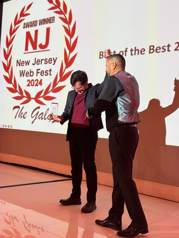 Roshan looking shocked while receiving the Best of the Best award from Neem Basha at New Jersey Web Fest 2024.