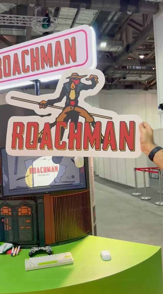A man holds up a sign that says "ROACHMAN" with the character of Roachman in hat, blue coat, and brown pants behind it.