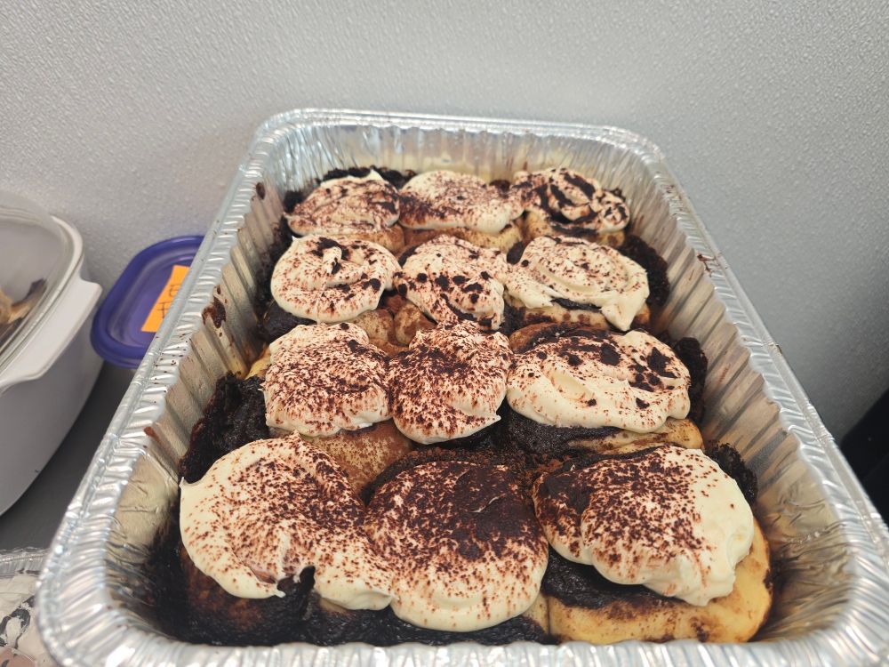 aluminum tray full of tiramisu cinnamon rolls covered in mascarpone icing and cocoa powder