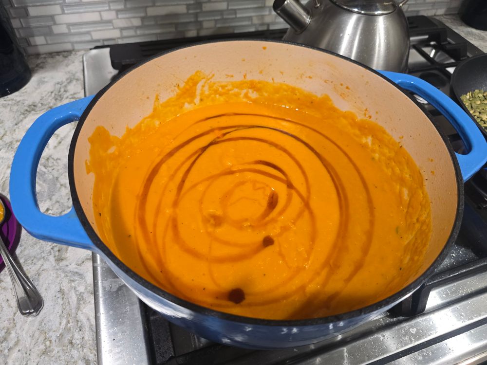 a blue dutch oven full of a light orange honeynut squash soup with a maple drizzle on top