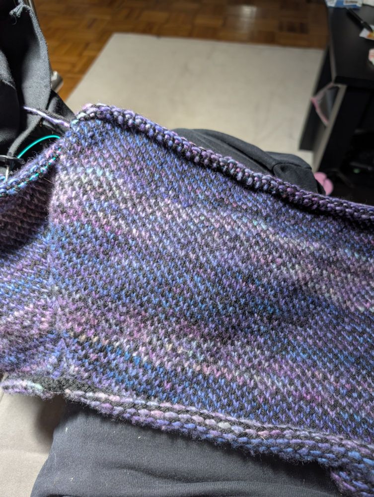 a hand knit sweater in alternating stripes of purples, blues, and greens