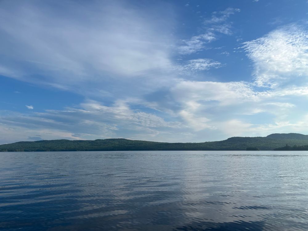 Picture from a lake with land and clouds in the distance 