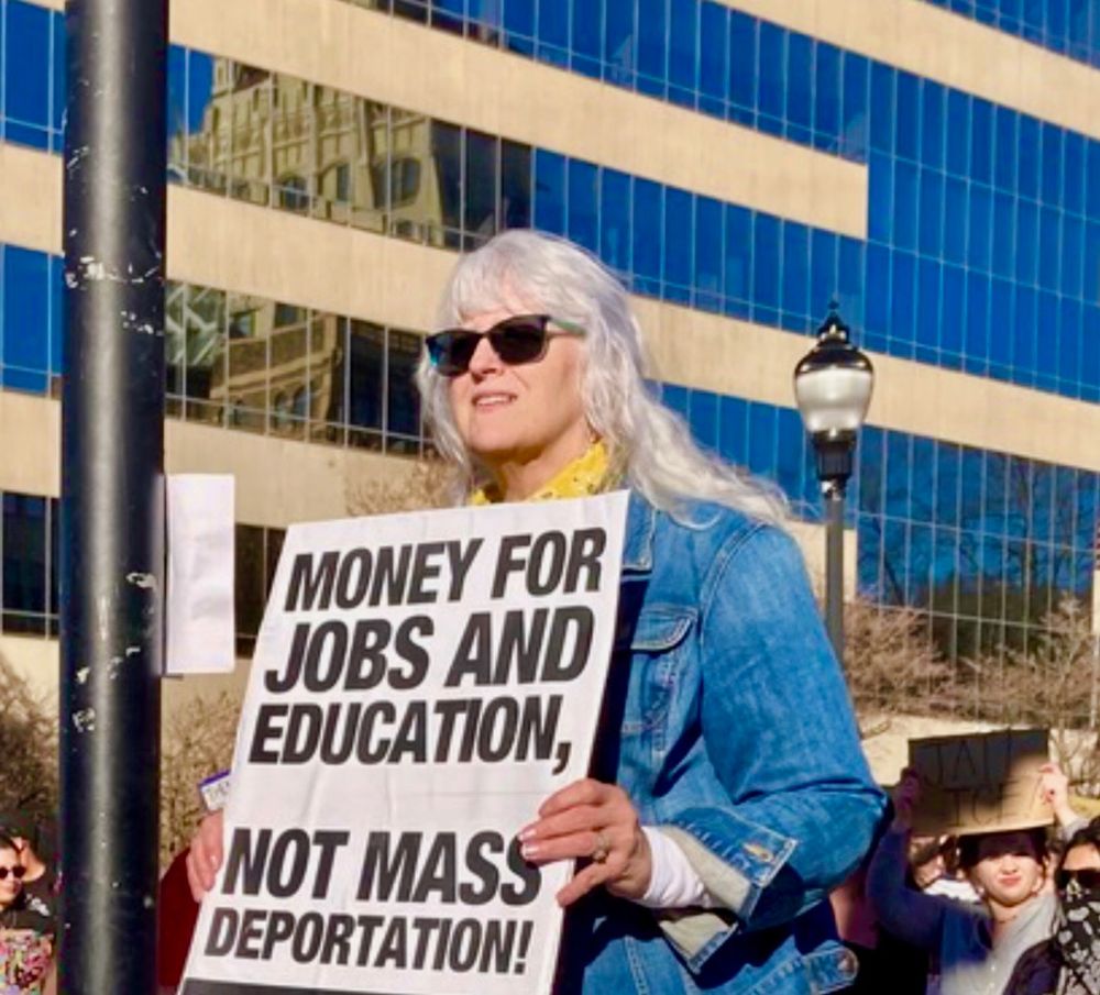 Woman carries a sign protesting ICE that read, "money for jobs and education not mass deportation."