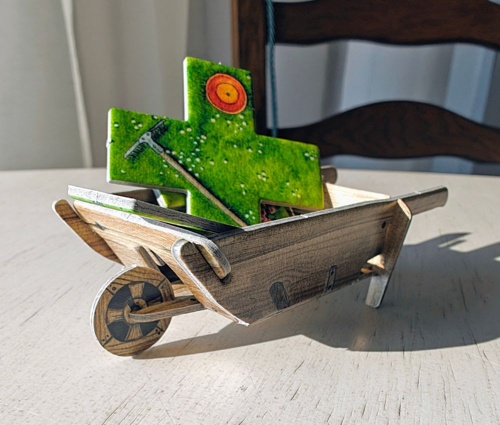 Cute little cardboard wheelbarrow carrying some flower tiles.