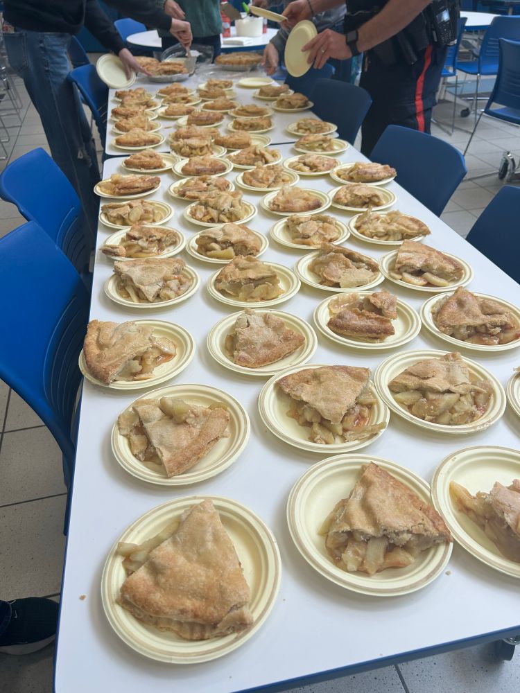 A white table is laden with slices of warm apple pie placed on beige paper plates 
