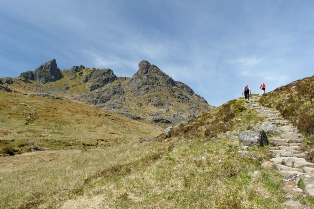 Walkers heading along constructed path towards rocky mountain.