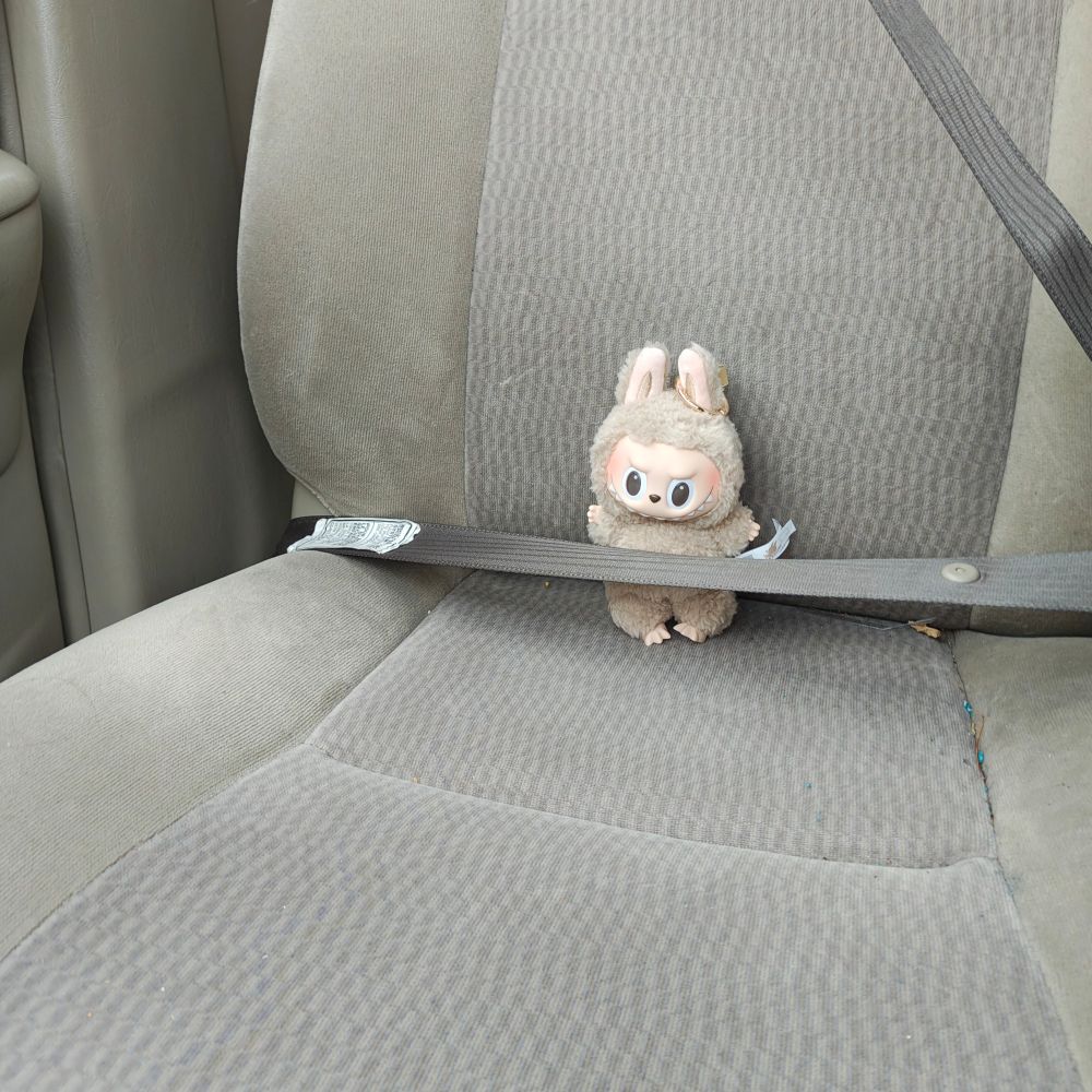 A toffee colored labubu buckled into the seat of a car