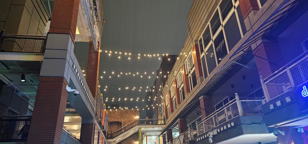 Strings of lights hang above as rain pours down. The boxed area with an abundance of walkways is silent.