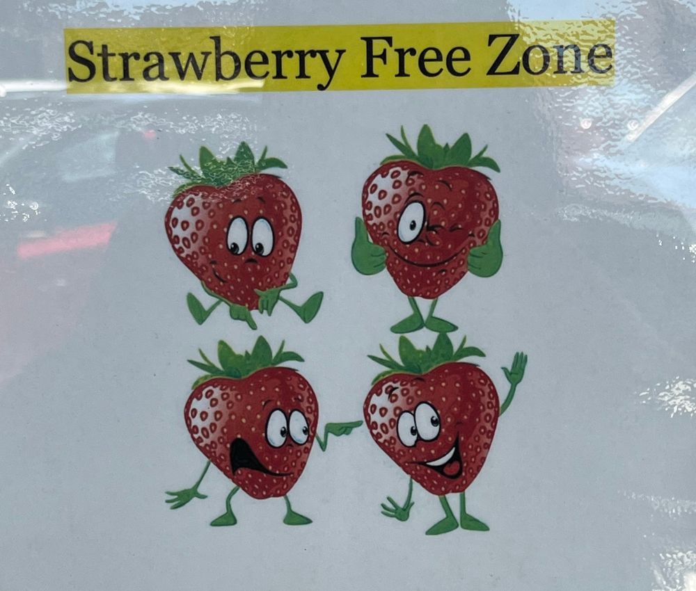 Sign with the text “Strawberry Free Zone”. Below are four strawberries with faces on them