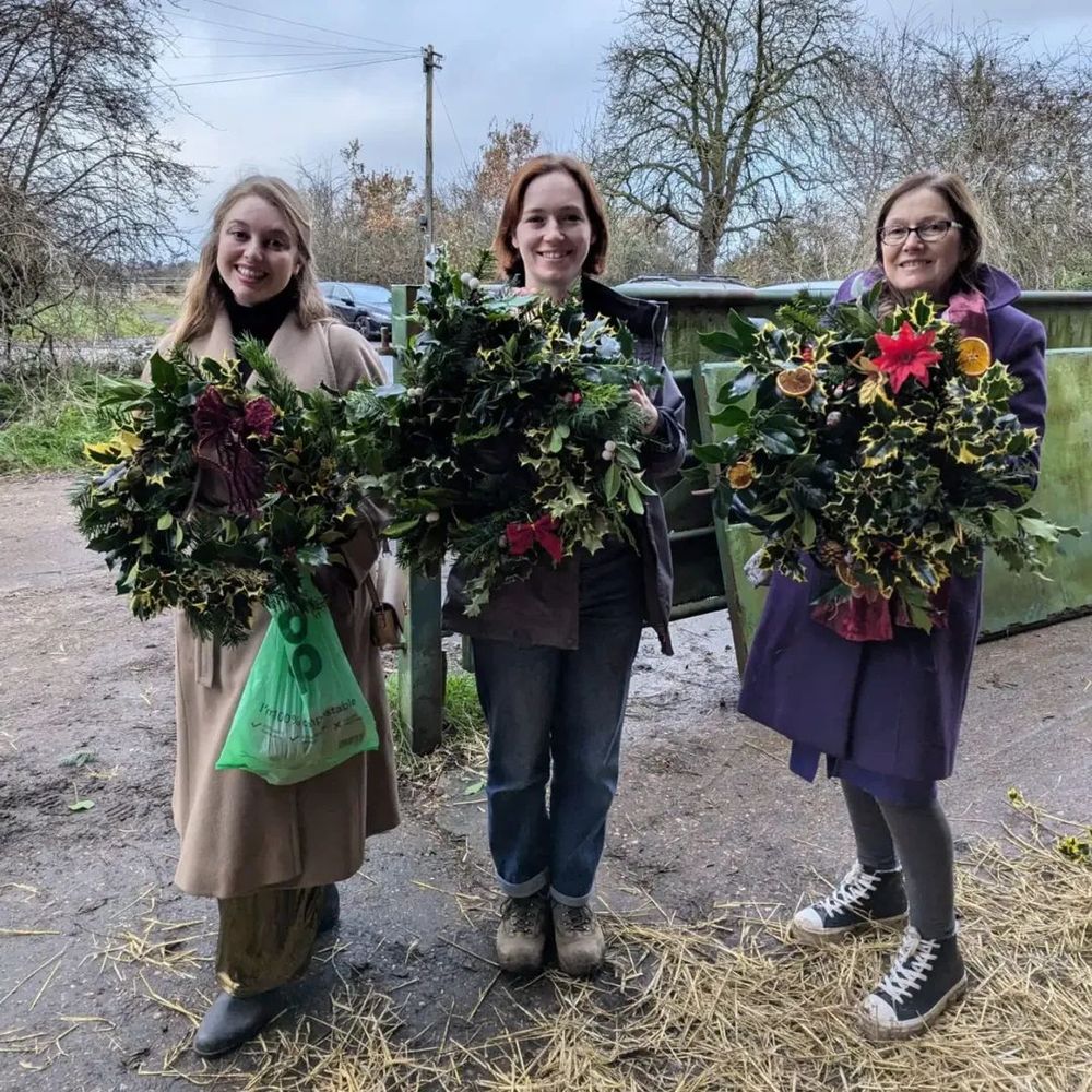 3 smiling people stand with their beautiful festive wreaths