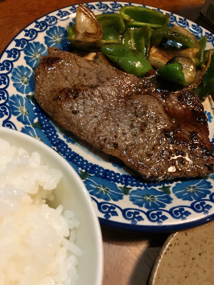 よく焼いた赤身のステーキと添えられた玉ねぎとピーマンの写真。手前には白ごはんもある。