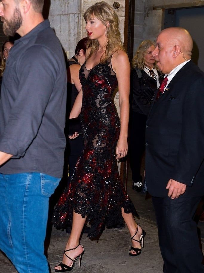 Taylor swift in a gorgeous black dress that had lots of see through black lace areas and is detailed with red. 