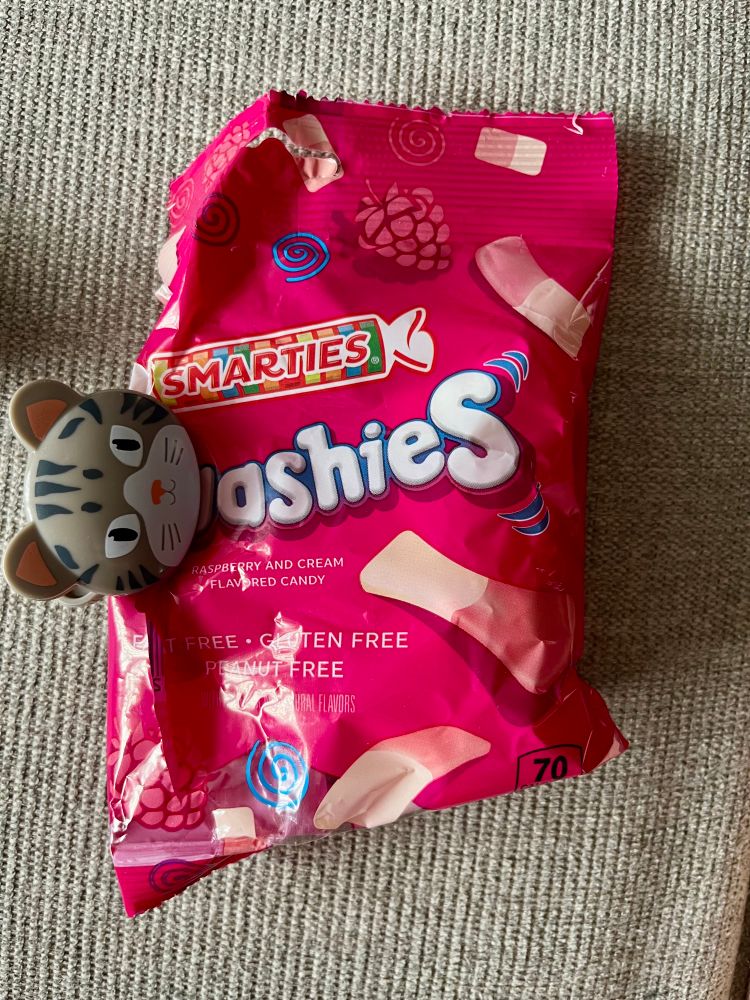 A pink bag of squashies candy with a bag clip that is shaped like a cat head on it 
