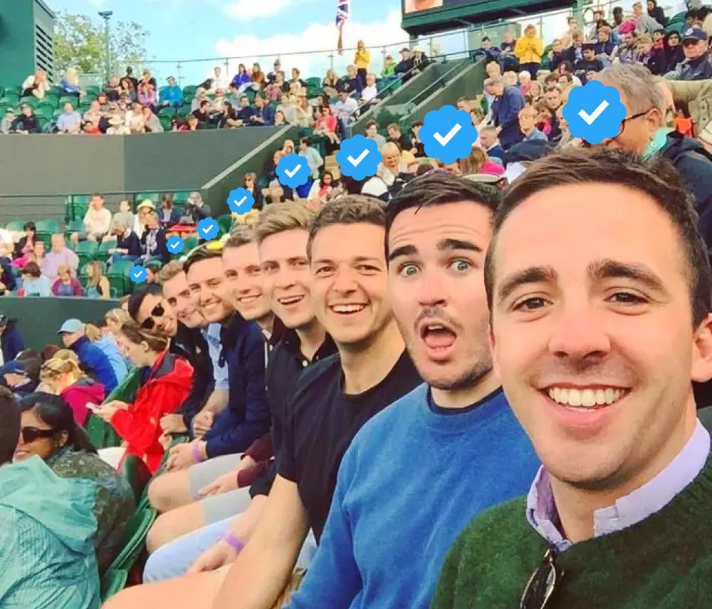 A row of white dudes all looking towards the camera that the front dude is holding. They're all in a stadium in a row, so each dude sits slightly more forward as you go down the row so their dumb face is visible.

I've added a blue check from Twitter to each of their heads.