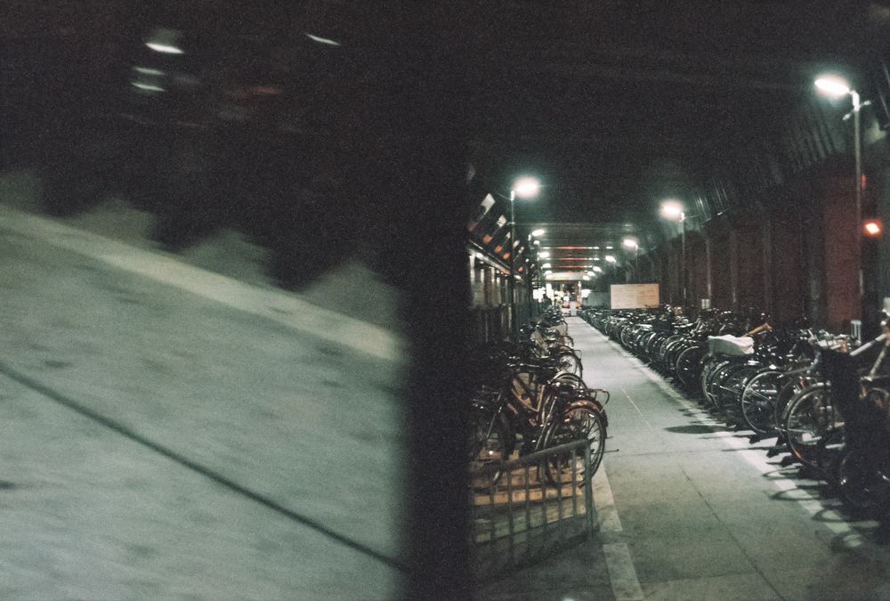 Split frame with two rows of bikes parked under bridge at night on right and motion blurred walkway on left in Nagoya, Japan.