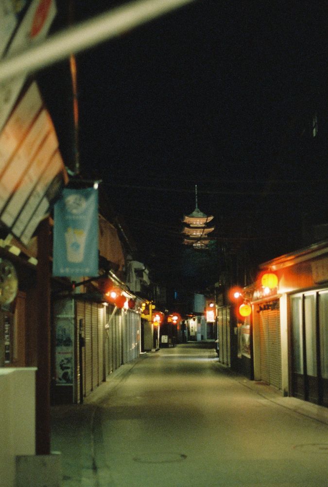 Closed shops with red lanterns lining empty street at night with pagoda in background.