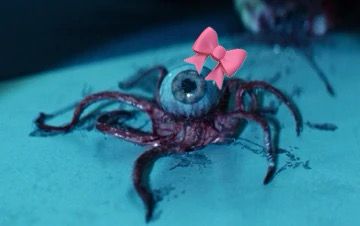An eyeball alien with red tentacle limbs. A sticker emoji of a pink now is above it 