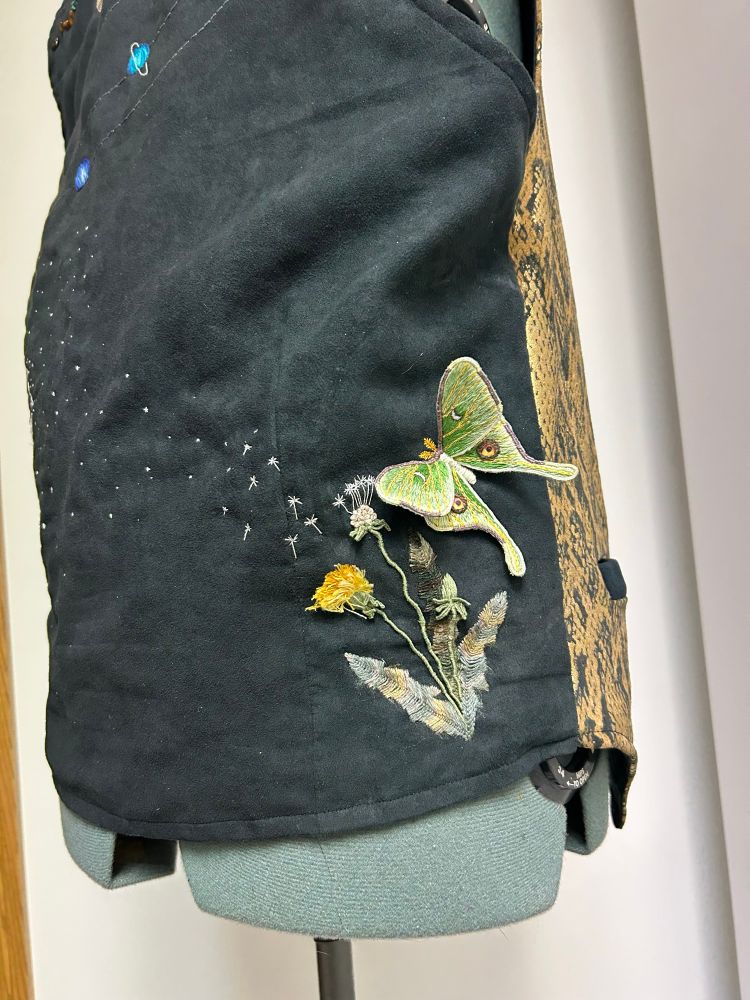 The back of a vest with a variety of embroidered details including a dandelion with seed blowing away and a Luna moth