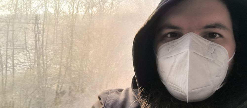 Im Bus mit Maske und im Hintergrund eine Winterlandschaft durch ein schmutziges busfenster