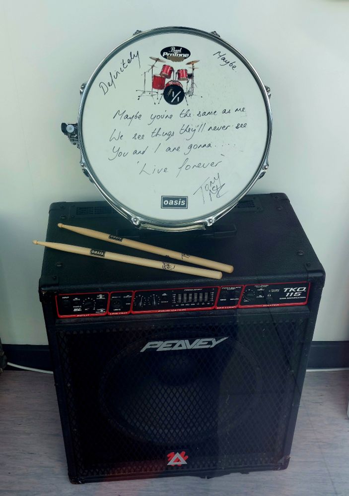 Drum and drum sticks on top of a Peavy Bass Amp. 
The drum skin is inscribed with the lyrics 
'Maybe you're the same as me
We see things they'll never see 
You and I are gonna 
Live Forever'
Signed Tony McC.