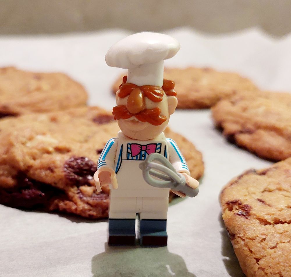 A LEGO Swedish Chef figure standing near freshly baked chocolate chip cookies.