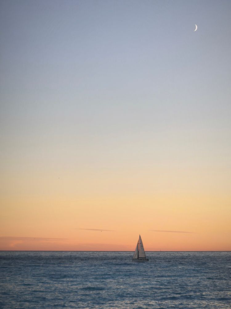 Croissant de Lune au dessus de la mer au coucher du soleil avec un voilier. 