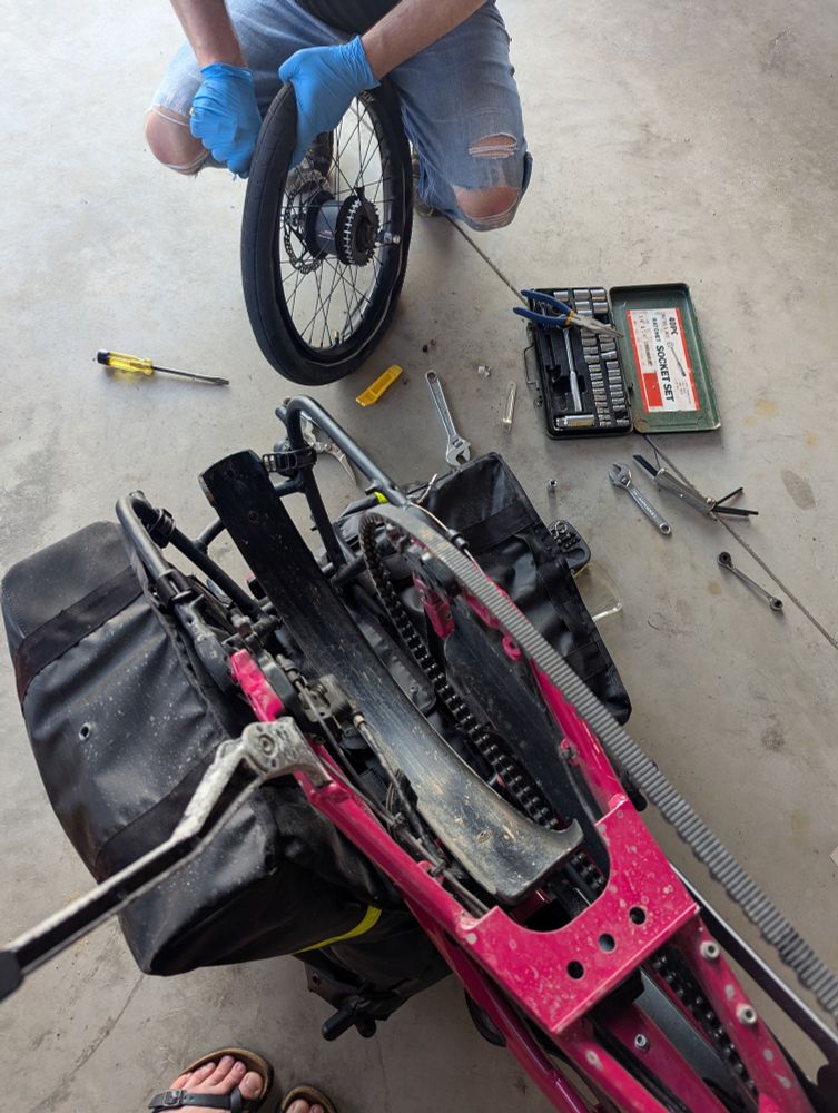 A bike flipped upside down with the back wheel removed. A person, only torso visible, holds the wheel while reinstalling the tire after a flat tube has been changed out.