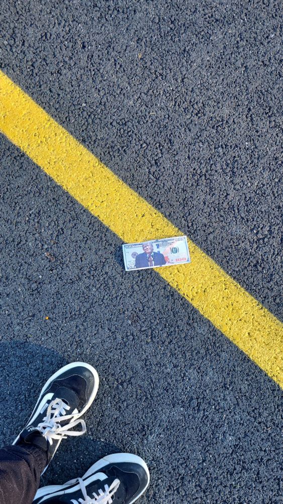 picture of an 100 dollar bill but with trump on it on the ground of a parking lot